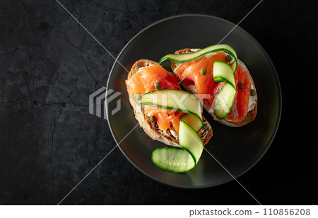 Sandwiches with smoked trout, cream cheese, fresh cucumber, and capers on a black plate. Sandwiches with smoked trout, cream cheese, fresh cucumber, and capers on a black plate. 110856208