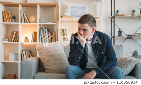 Frustration depression. Bad mood. Sad unhappy desperate pensive man with negative thoughts sitting on couch at home in living room copy space. 110856914