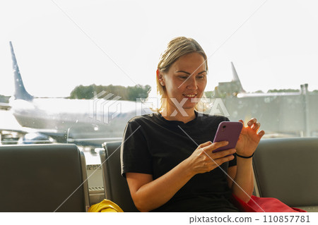 Airport terminal. Woman waiting for flight using smartphone. Girl with cell phone in airport surfing internet social media apps. Traveling female in boarding lounge of airline hub. Traveling girl 110857781