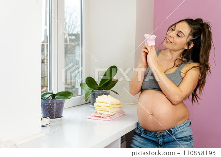 Pregnant woman with neatly folded baby clothes joy of preparing for motherhood. Pregnant woman with neatly folded baby clothes joy of preparing for motherhood. 110858193