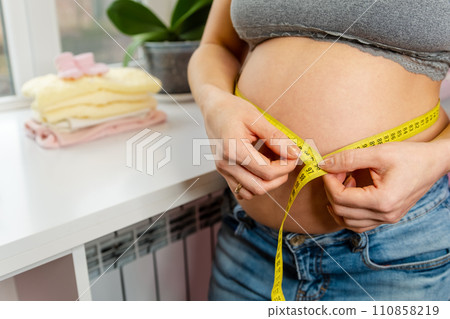 A pregnant woman measuring her belly with a yellow tape measure 110858219