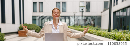 Woman freelancer working on laptop while sitting outside in lotus position on office background Woman freelancer working on laptop while sitting outside in lotus position on office background 110858935
