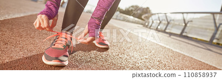 Being prepared. Cropped shot of active mature woman wearing sportswear tying her shoe laces while getting ready for running outdoors on a sunny day 110858937