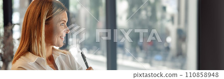Smiling mature business woman standing with crossed hands in modern coworking and looking at side 110858948