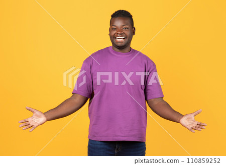 Cheerful Black Guy In Purple T-Shirt Spreading Arms, Yellow Backdrop Cheerful Black Guy In Purple T-Shirt Spreading Arms, Yellow Backdrop 110859252