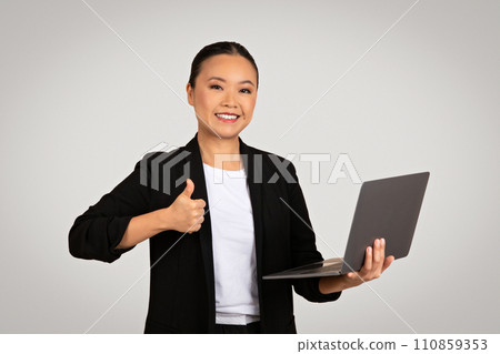 Cheerful Asian businesswoman holding a laptop with one hand and giving a thumb up 110859353