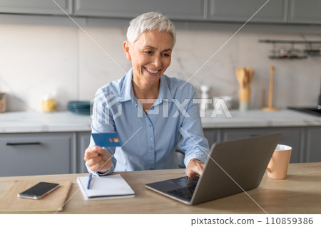 Senior Lady Holding Credit Card Using Laptop At Home Kitchen 110859386