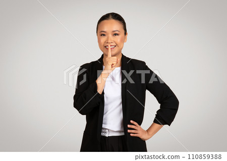 Professional Asian businesswoman with a secretive expression placing a finger to her lips 110859388