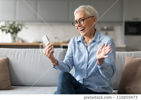 Excited mature woman in eyewear reading news on cellphone indoor 110859473