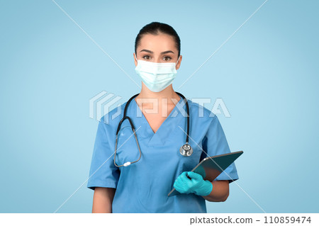 Confident young woman doctor, nurse in blue uniform , protective mask and gloves holding clipboard, blue background 110859474