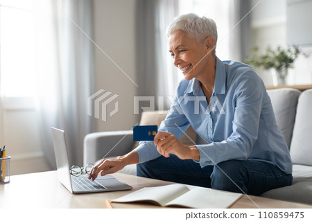 senior lady with credit card websurfing laptop for purchases indoors 110859475