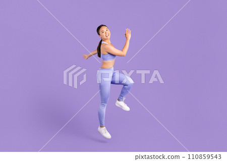 Joyful asian woman in activewear running in place on purple backdrop Joyful asian woman in activewear running in place on purple backdrop 110859543