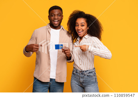 Joyful black couple pointing at credit card on yellow background Joyful black couple pointing at credit card on yellow background 110859547