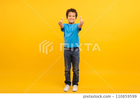 Boy in blue t-shirt giving thumbs up on sunny yellow background 110859599