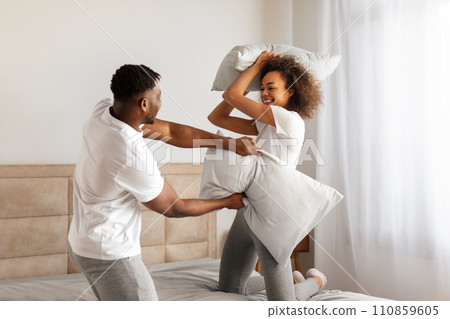 Playful loving black couple enjoys carefree pillow fight in bedroom Playful loving black couple enjoys carefree pillow fight in bedroom 110859605