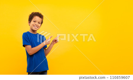 Latin boy with bright smile pointing at copy space against yellow backdrop 110859607
