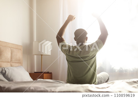 black guy sitting on bed indoor stretching body and arms black guy sitting on bed indoor stretching body and arms 110859619