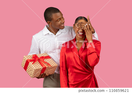 Black man surprises woman with gift, covering her eyes, both in formal attire 110859621