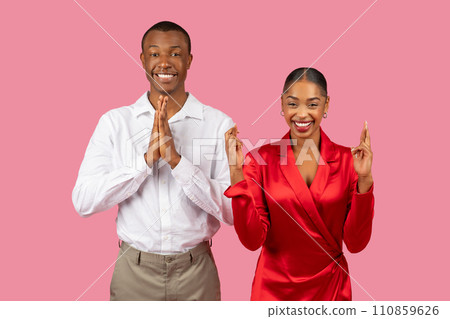Black man and woman in prayer pose and crossing fingers, hopeful smiles, pink background Black man and woman in prayer pose and crossing fingers, hopeful smiles, pink background 110859626