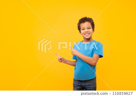 Joyful boy pointing to side at copy space, wearing blue t-shirt, yellow backdrop Joyful boy pointing to side at copy space, wearing blue t-shirt, yellow backdrop 110859627