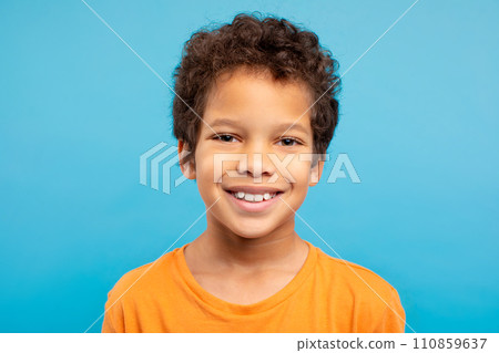 Cheerful curly-haired boy in orange t-shirt, blue background 110859637