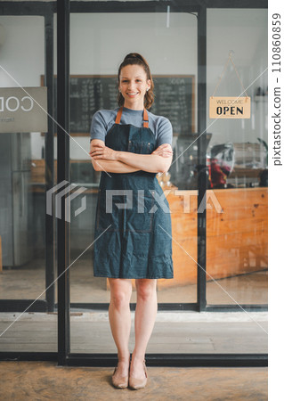 Portrait of happy waitress standing at restaurant entrance with open sign, Portrait of young business woman attend new customers in her coffee shop. 110860859