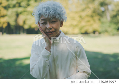A woman in her 60s in a park with a toothache 110861997