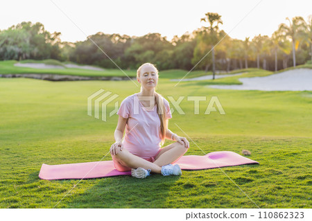 Energetic pregnant woman takes her workout outdoors, using an exercise mat for a refreshing and health-conscious outdoor exercise session 110862323