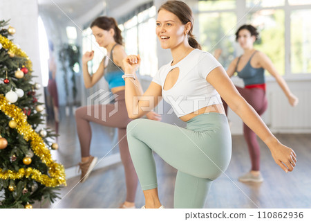 Cheerful young female fitness instructor leading Zumba class in Christmas studio Cheerful young female fitness instructor leading Zumba class in Christmas studio 110862936