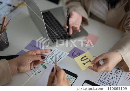 A meeting table with a team of creative UI UX graphic designers working on a mobile app prototype. 110863109