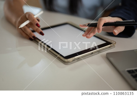 Cropped shot of two Asian women are discussing work and using a digital tablet in the office. Cropped shot of two Asian women are discussing work and using a digital tablet in the office. 110863135