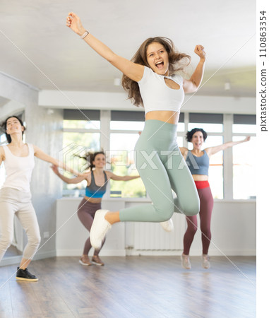 Girls engaged shake leg in dance fitness hall with friends, group of youthful people jumped into air Girls engaged shake leg in dance fitness hall with friends, group of youthful people jumped into air 110863354