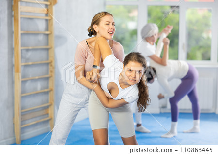 Woman and girl in gym perform basic elements of krav maga self-defense system. 110863445