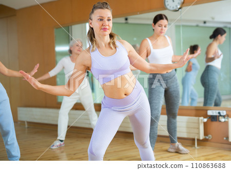 Energetic women amateur dancers of different ages moving leg to side at lesson with coach in dance hall 110863688