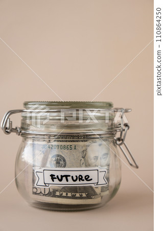 Saving Money In Glass Jar filled with Dollars banknotes. FUTURE transcription in front of jar. Managing personal finances extra income for future insecurity Saving Money In Glass Jar filled with Dollars banknotes. FUTURE transcription in front of jar. Managing personal finances extra income for future insecurity 110864250