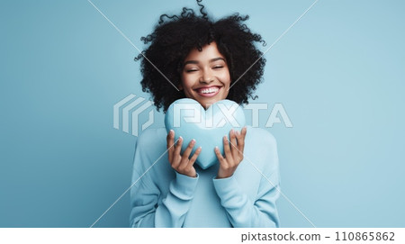 Beautiful African American woman holding and hugging big blue heart on blue background. St Valentine's Day vibe. Beautiful African American woman holding and hugging big blue heart on blue background. St Valentine's Day vibe. 110865862
