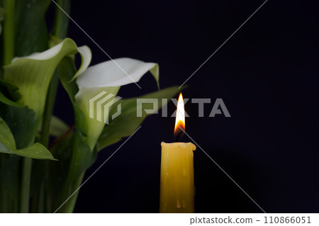 Burning wax candle and white calla lily flowers in darkness Burning wax candle and white calla lily flowers in darkness 110866051