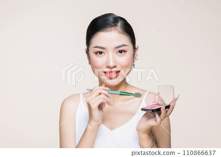 Young asian smiling woman holding blush palette with a brush isolated on a beige background Young asian smiling woman holding blush palette with a brush isolated on a beige background 110866637