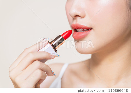 pretty asian woman using a red lipstick on beige background pretty asian woman using a red lipstick on beige background 110866648