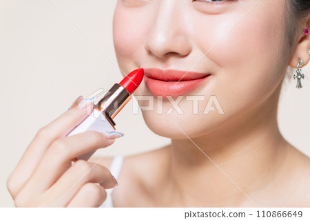 Young woman applying lipstick on beige Young woman applying lipstick on beige 110866649