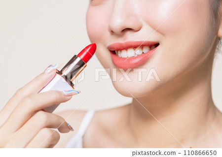pretty asian woman using a red lipstick on beige background pretty asian woman using a red lipstick on beige background 110866650
