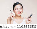 Beautiful asian young woman holding mascara and smiling on purple studio background, 110866658