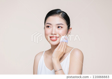 Young asian woman smile looking happy applying makeup with puff makeup on beige background. Young asian woman smile looking happy applying makeup with puff makeup on beige background. 110866663