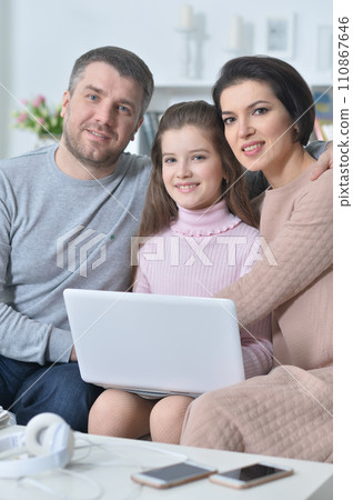 Happy girl sitting at table with laptop with her parents Happy girl sitting at table with laptop with her parents 110867646