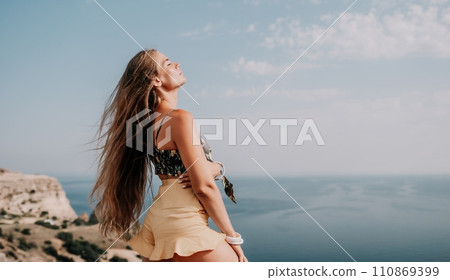 Woman travel sea. Happy tourist taking picture outdoors for memories. Woman traveler looks at the edge of the cliff on the sea bay of mountains, sharing travel adventure journey 110869399