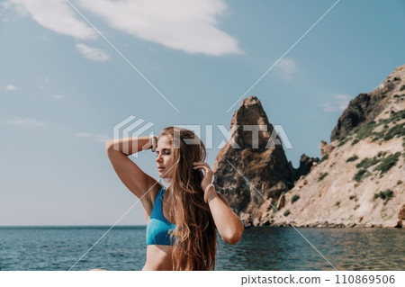 Woman summer travel sea. Happy tourist enjoy taking picture outdoors for memories. Woman traveler posing on the beach at sea surrounded by volcanic mountains, sharing travel adventure journey 110869506