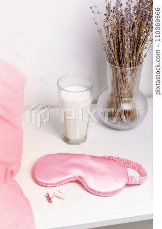Bedside table with a silk sleep mask, earplugs and lavender and warm milk for a good night's sleep. All conditions for good deep sleep. Help for falling asleep. Vertical nude photo 110869866
