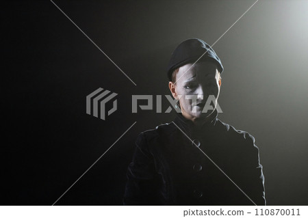Minimal portrait of sad mime standing on stage in contour lighting against black background, copy space 110870011