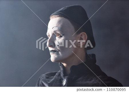 Dramatic headshot portrait of mime artist standing on stage in spotlight and looking away with sad face makeup, copy space 110870095