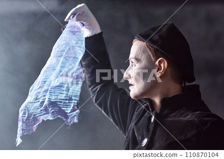 Dramatic side view portrait of mime artist performing on stage and holding shimmering cloth to light, copy space 110870104